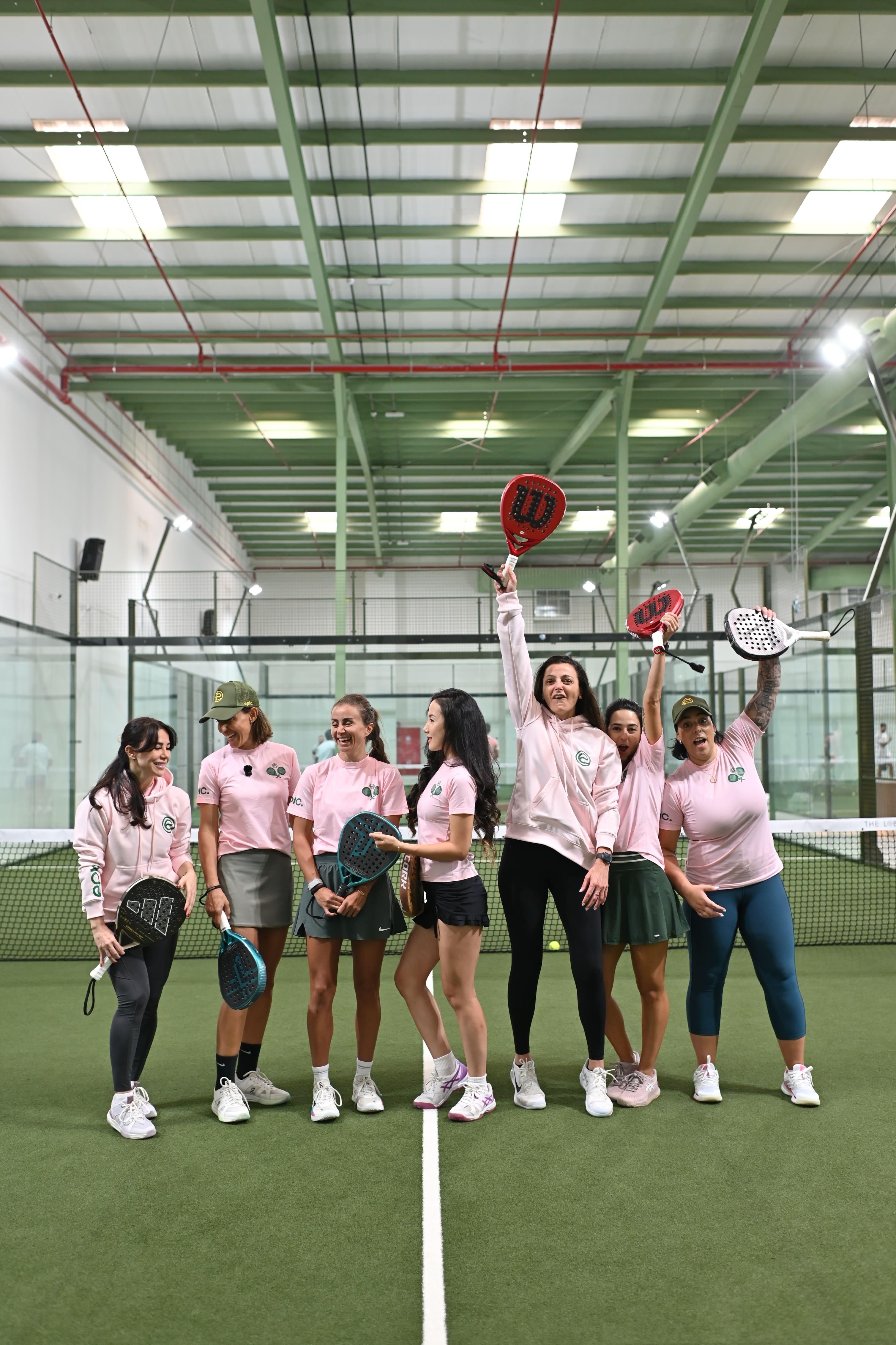 Group of women holding padel rackets on an indoor court at Epic Padel Charlotte, wearing matching pink shirts, celebrating the grand opening event.